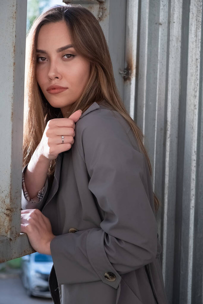 attractive young asian model in gray trench coat standing near metal fence - Zdjęcie, obraz