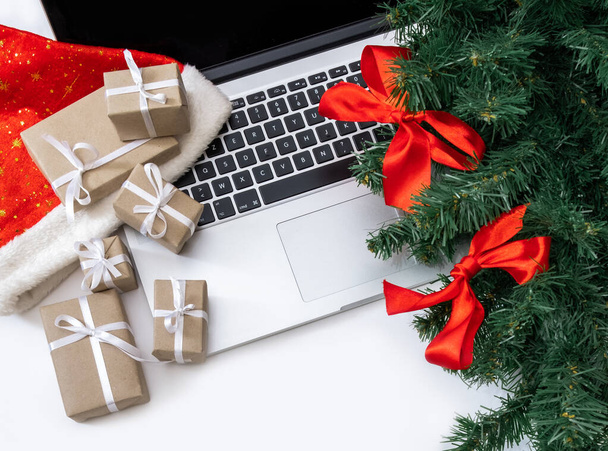 Ordinateur portable avec cadeaux, chapeau rouge, arbre de Noël et boîtes d'emballage sur le fond blanc, vue du dessus, concept de livraison. - Photo, image