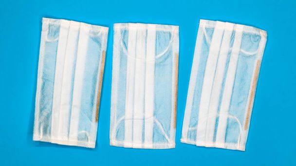 Drie wegwerp chirurgische gelaatsmaskers met rubberen kussens om de mond en neus te bedekken op een blauwe achtergrond. Het concept van bescherming tegen bacteriën, gezondheidszorg en geneeskunde. COVID-19. Gevaarlijk virus. - Foto, afbeelding