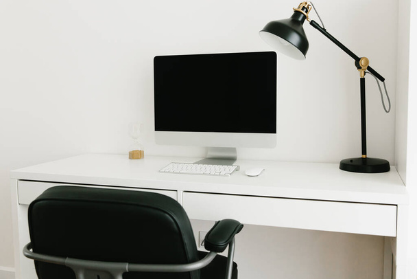 Weißer Schreibtisch mit schwarzem Monitor, Schreibtischlampe und Stuhl. Arbeitsplatzkonzept. Minimalismus im Innenraum. Arbeit von zu Hause aus, studentischer Arbeitsplatz. - Foto, Bild