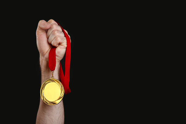 Man holding golden medal on black background, closeup. Space for design - Фото, изображение