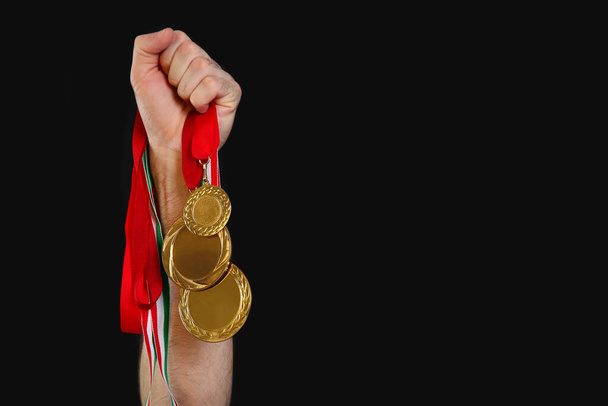 Man holding golden medals on black background, closeup. Space for design - Φωτογραφία, εικόνα