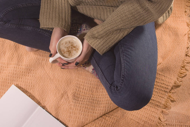 Örülmüş kış çorapları ve beyaz sıcacık çorapları olan bir kadın ekoseye oturur ve kışın evde sıcak kakao ile ısınır. Sıcak zaman ve kış içkileri - Fotoğraf, Görsel
