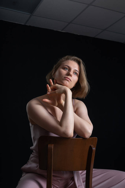 woman with short hair posing in pink suit, sitting on chair on black background - Fotoğraf, Görsel