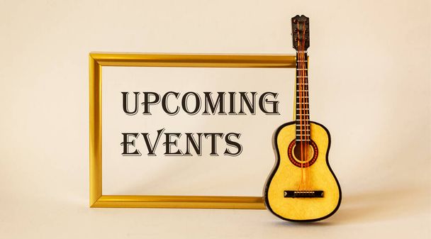 Nadcházející událost zpráva na zlatém rámečku s hračkou kytara na bílém pozadí - Fotografie, Obrázek
