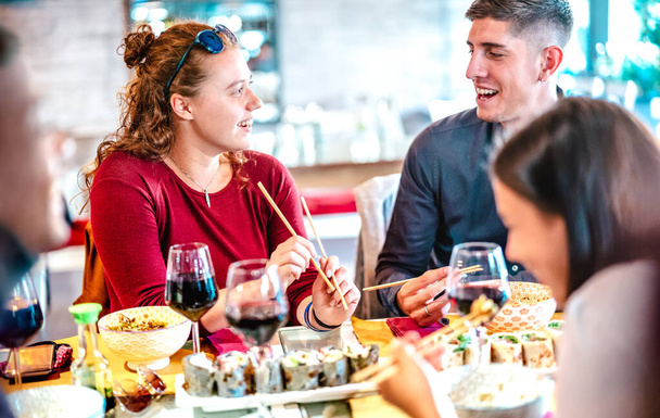 Couple heureux jouant avec des baguettes au restaurant du bar à sushi - Concept de style de vie alimentaire avec des gens heureux s'amusant ensemble manger et boire du vin - accent sélectif sur la femme aux cheveux roux - Photo, image