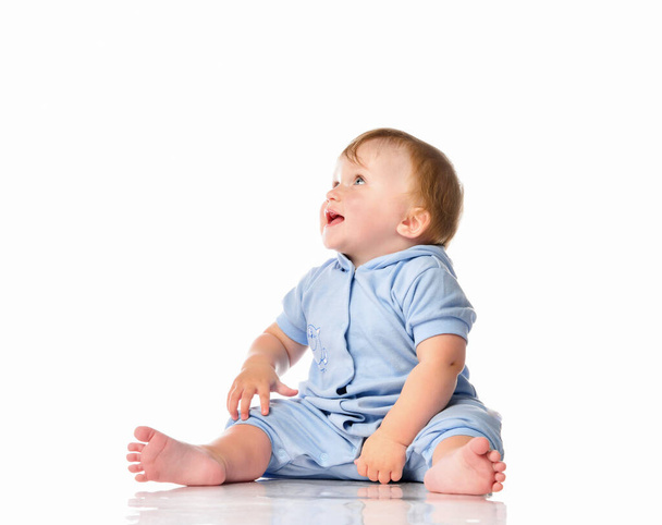 Baby in blue jumpsuit sitting on floor looking up - Photo, image