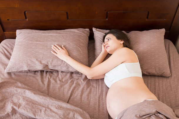 όμορφη νεαρή έγκυος γυναίκα ξαπλωμένη στο κρεβάτι, με θέα στην κορυφή. Το κορίτσι υποφέρει από το γεγονός ότι ο σύζυγός της την άφησε, - Φωτογραφία, εικόνα