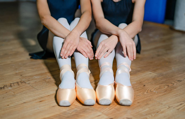 Two ballet girls put on pointe shoes while sitting on the wooden floor. Ballet dancers tyied ballet shoes. Close-up - Фото, зображення