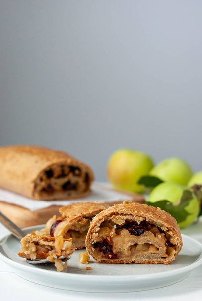 Homemade apple strudel with fresh apples and cranberries on a white wooden table. - Foto, afbeelding
