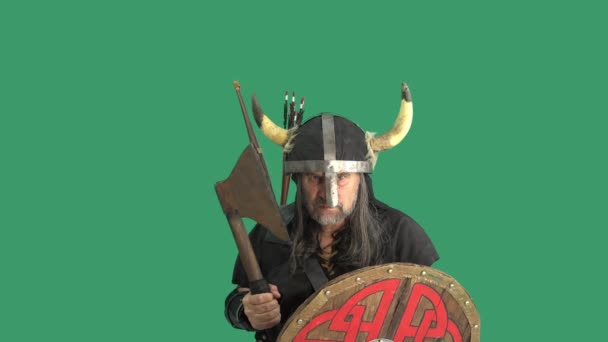 Portrait de guerrier mâle mature, Viking dans un casque avec des cornes, des cris et des vagues agressives grande hache et frappe avec colère bouclier en bois avec elle. Fond vert - Séquence, vidéo