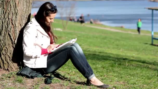 Happy female student doing homework in city park.Happy female student reading book in city park. - Кадри, відео