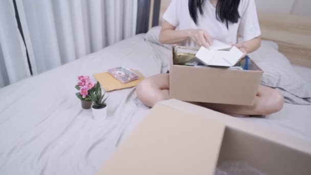 Азіатська молода жінка сідає всередину спальні, переїжджаючи на нове місце з картонною коробкою на колінах, роблячи старе фото з коробки в нову квартиру, сортування прибирання, переміщення пам'яті, що рухається - Кадри, відео