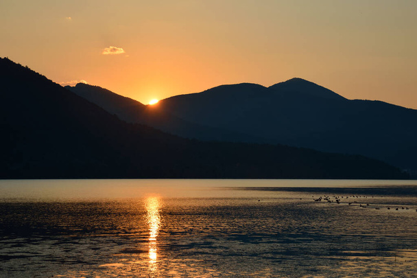 Paisaje escénico de crestas montañosas y rayos de sol reflejándose en las aguas del lago a la hora dorada - Foto, imagen