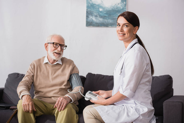 geriatric nurse examining aged man with tonometer at home - 写真・画像