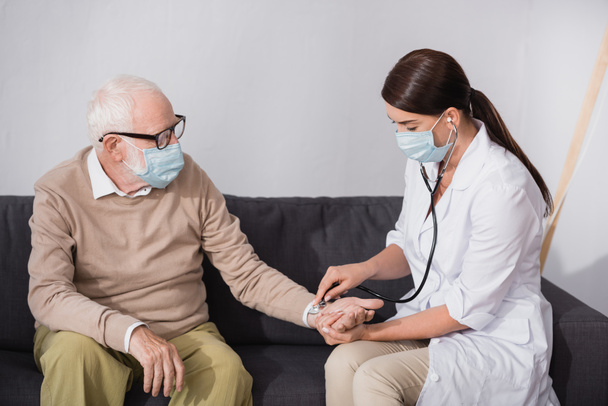 брюнетка медсестра перевіряє тиск літнього чоловіка зі стетоскопом
 - Фото, зображення
