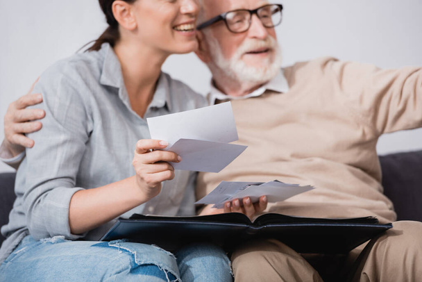 улыбающаяся женщина смотрит на фотографии, сидя рядом с пожилым отцом на размытом фоне - Фото, изображение