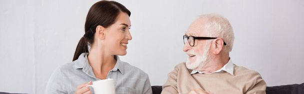 cheerful woman with cup of tea talking to happy elderly father, banner - Photo, Image