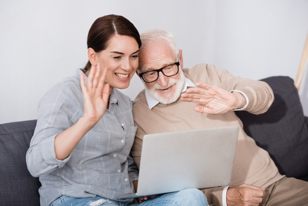 alegre anciano hombre con hija saludando las manos mientras tiene video chat en el ordenador portátil - Foto, Imagen