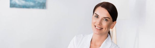 allegra infermiera bruna in camice bianco sorridente alla macchina fotografica, banner - Foto, immagini
