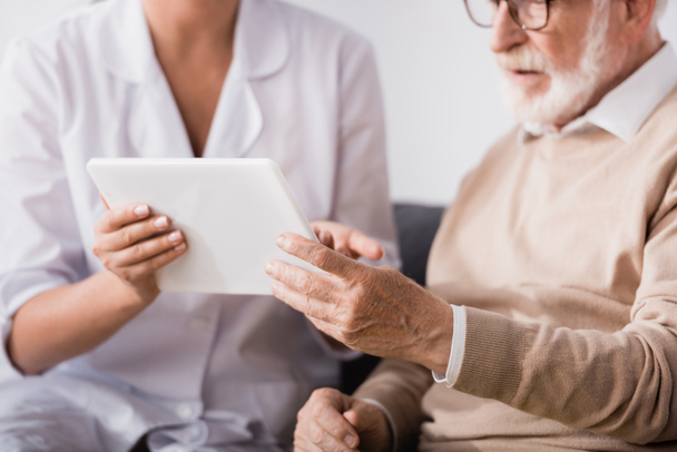 cropped of social worker showing digital tablet to aged man at home - Foto, Bild