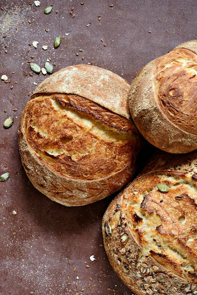 Домашний свежеиспеченный сельский хлеб из пшеницы и цельной зерновой муки на коричневом фоне. Французский свежеиспеченный хлеб.  - Фото, изображение
