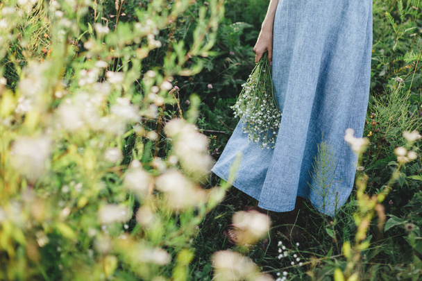 Girl in light blue linen dress with bunch of wildflowers on a summer meadow in sunlight.  Summer background.   - Fotoğraf, Görsel