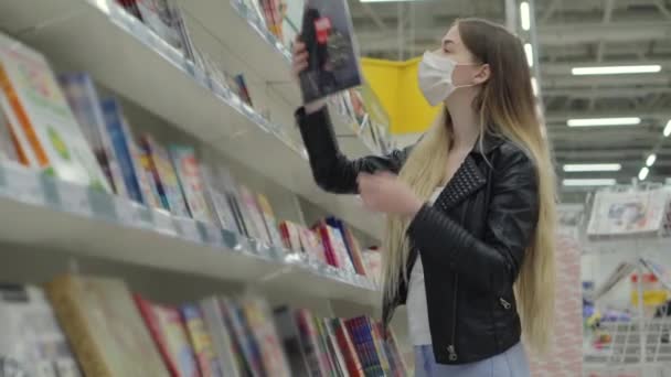 Giovane femmina in mascherina medica acquisto rivista in supermercato - Filmati, video