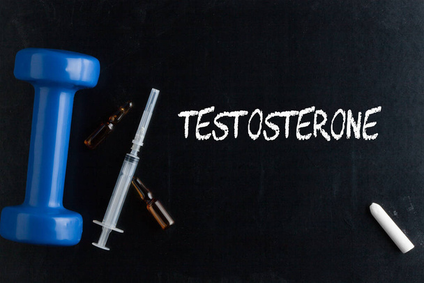 Слово тестостерон написано мелом и гантели, шприц и ампула на доске. - Фото, изображение