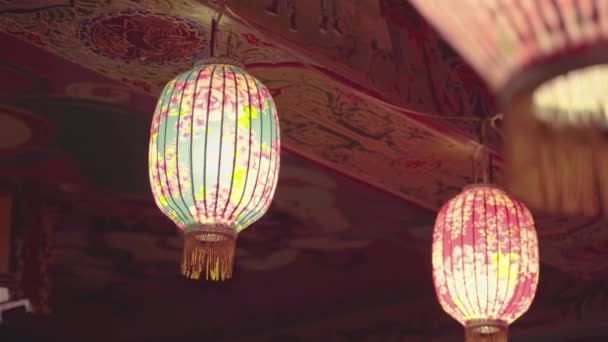 Een close-up camera take van kleurrijke lantaarns met bloemen patroon op opgehangen op het dak van een tempel. De lantaarns verspreiden een warm gevoel in de nacht. - Video
