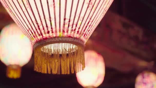 Een rose lantaarn met bloemen patroon erop hing op het dak van een tempel, langzaam schuddend in een diepe nacht. De lantaarns verspreiden een warm gevoel in een Chinees interieur. - Video