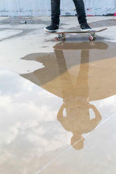 Reflexión en un charco de agua de un niño montando un monopatín en un parque de skate en Bogotá, Colombia - Foto, imagen