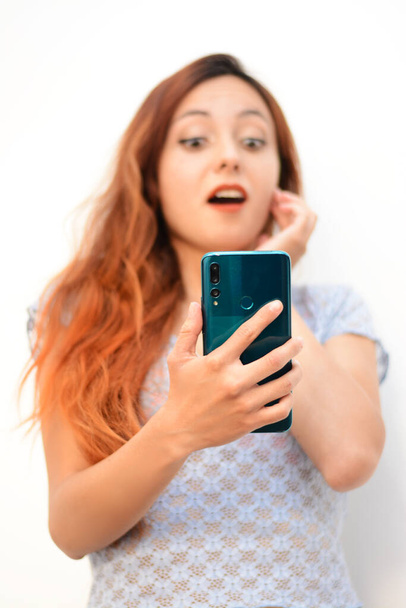 Surprised girl texting talking looking at mobile phone open mouth, red head woman looking at cellphone profile view. white background - Foto, immagini