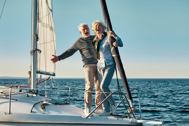 Чувствуем себя счастливыми вместе. Полная длина взволнованных мужчина и женщина в отставке, старшая влюбленная пара, стоящая на борту яхты, плавающая в море, обнимающая и смеющаяся - Фото, изображение