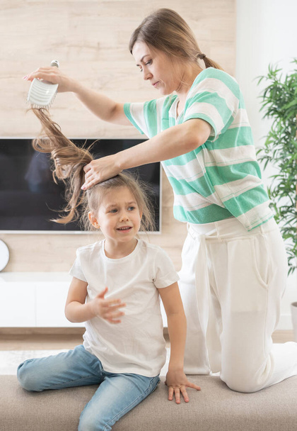 mother tidy up daughters hair. girl doesnt want to have her hair brushed. close up photo. kid feels bad, because mother pulls her hair - Photo, Image