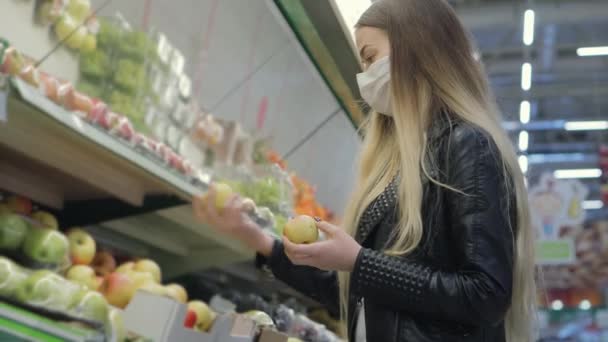 mulher com máscara facial está comprando maçãs no supermercado, epidemia - Filmagem, Vídeo