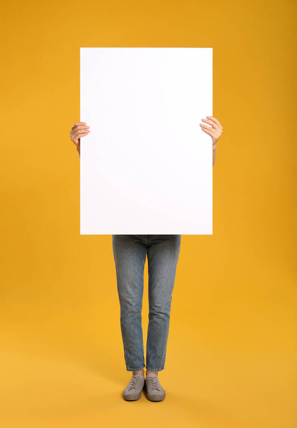 Woman holding white blank poster on yellow background. Mockup for design - Valokuva, kuva