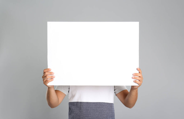 Man holding white blank poster on grey background. Mockup for design - Foto, Imagem