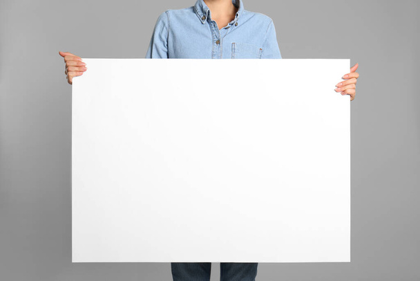 Woman holding white blank poster on grey background, closeup. Mockup for design - Photo, Image