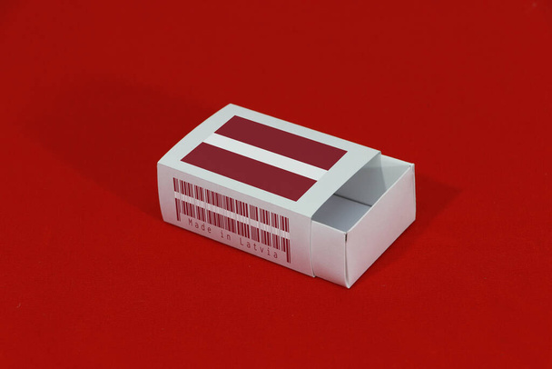 Латвійський прапор на білій коробці з баркодом і кольором державного прапора на червоному тлі, пакування паперу для розміщення сірників або продуктів. Концепція експорту з Латвії. - Фото, зображення