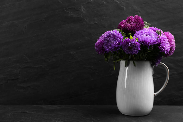 Beautiful asters in jug on table against black background, space for text. Autumn flowers - Foto, Imagem