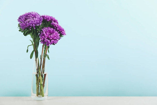 Beautiful asters in vase on table against light blue background, space for text. Autumn flowers - Photo, Image