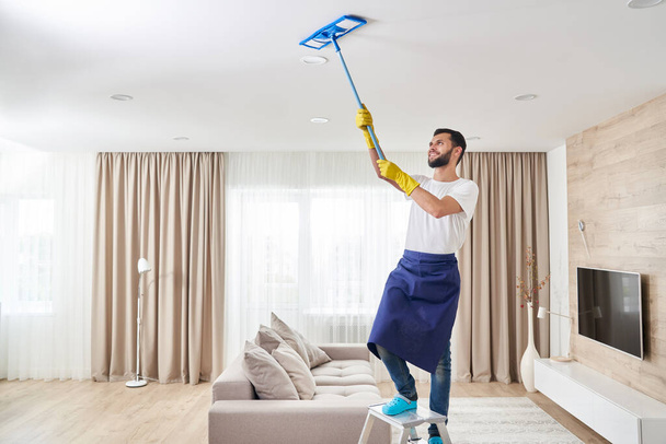 Uomo pulizia soffitto e lampade in soggiorno. Servizio di pulizia della casa concetto. - Foto, immagini