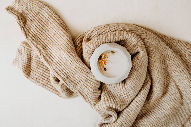 candle with dried flowers in concrete vase wrapped in cozy beige knitted sweater ona white background, selective focus - Fotografie, Obrázek