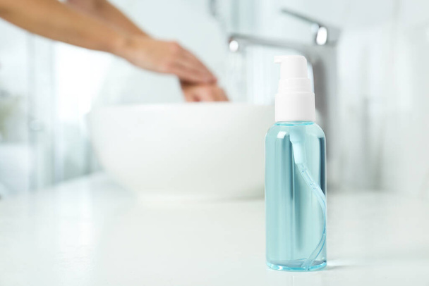 Bottle of antibacterial soap and blurred woman washing hands on background. Personal hygiene during COVID-19 pandemic - Photo, Image