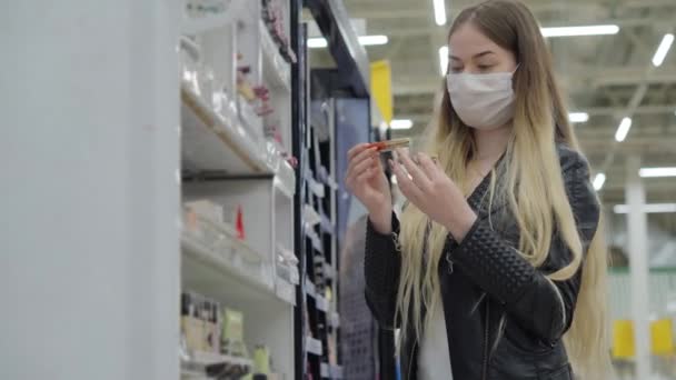Fiatal nő orvosi maszkban szájfényt vásárol a szupermarketben - Felvétel, videó