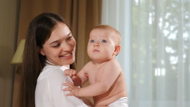 Gelukkige jonge moeder die naar haar baby kijkt. Concept van kinderen, baby, ouderschap, jeugd, leven, moederschap en moederschap. Mooie glimlachende baby. 4 k video - Video