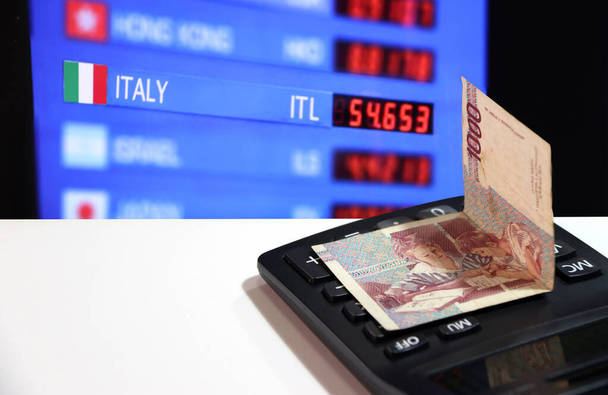 One thousand Lire of Italy banknote on the calculator on white floor with digital board of currency exchange money background, Lire Italia money the concept of finance. - Photo, Image