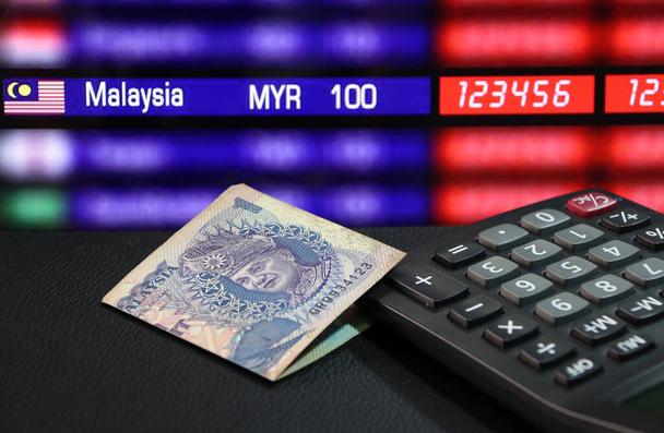 Un billet de banque ringgit de Malaisie et calculatrice sur le sol noir avec tableau numérique de monnaie de change arrière-plan, le concept de la finance. - Photo, image