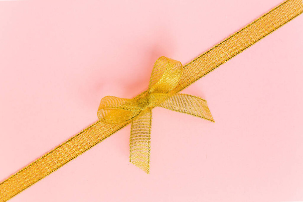 Gold ribbon with bow, isolated on pink background. Colorful celebration, birthday background. Flat lay, top view - Fotoğraf, Görsel